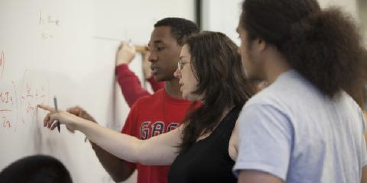Students standing at whiteboard working on an equation