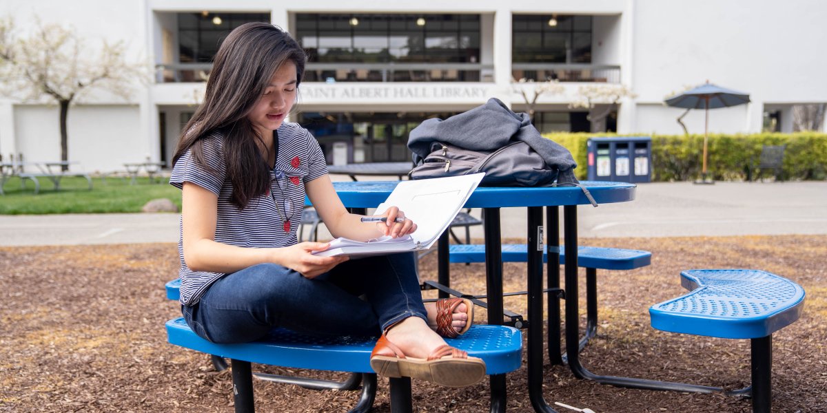 A student studying on a bench in the middle of SMC's campus