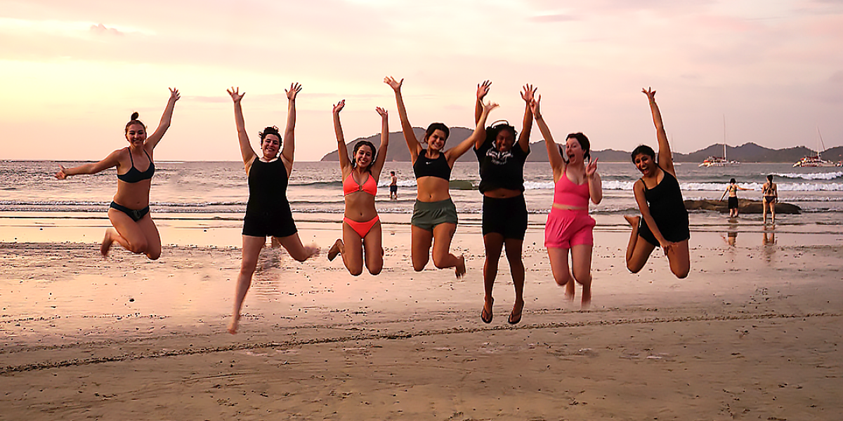 Students jumping on a beach in front of a sunset
