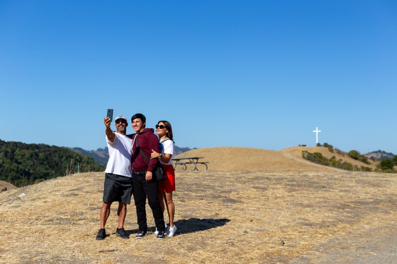A student and his parents take a selfie with The Cross far in the background