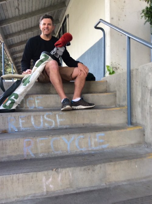 Josh Smith sits on a schoolyard stairs reading: Reuse, Recycle