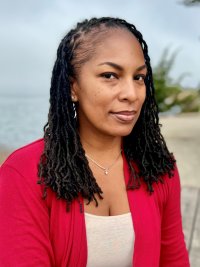 Headshot for Kimberly Ridgeway dressed in a white top under a red cardigan with an outdoor seascape as the background