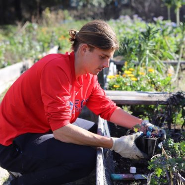 male presenting student gardening at the legacy garden