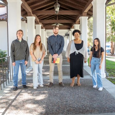 Science students posing with mentor in outdoor hallway