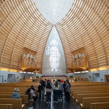 Studentsstand in the aisle of a large cathedral of light wooden slats in Oakland, CA.