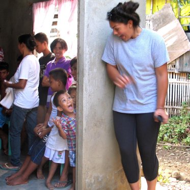 A student plays peekaboo around an open door with a small child. Both are laughing.