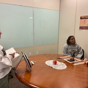 two women are sitting and talking where one lady is looking at them 