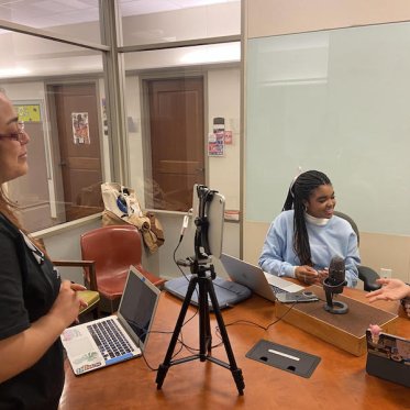 two women are sitting and talking where one lady is looking at them 