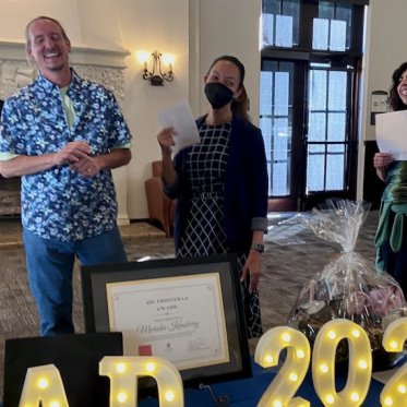 three people holding papers and one of the man is giving a speech
