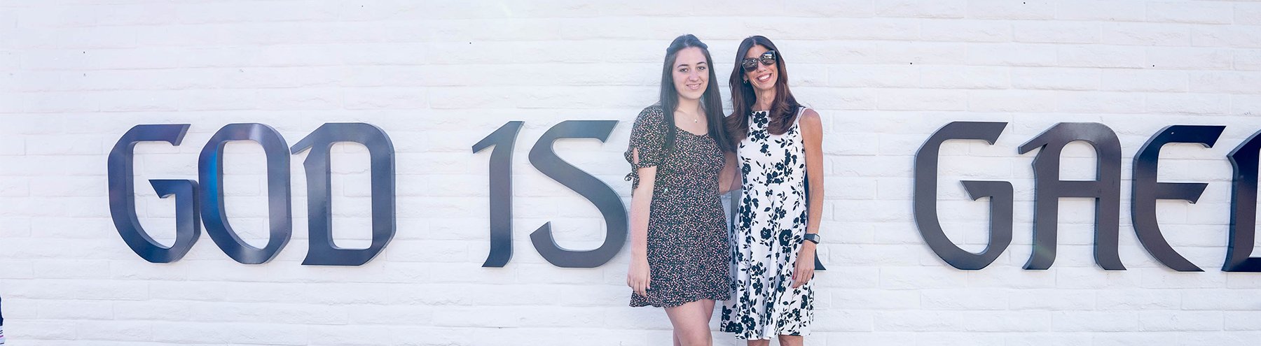 Two people pose in front of a SMC sign that says God is a Gael