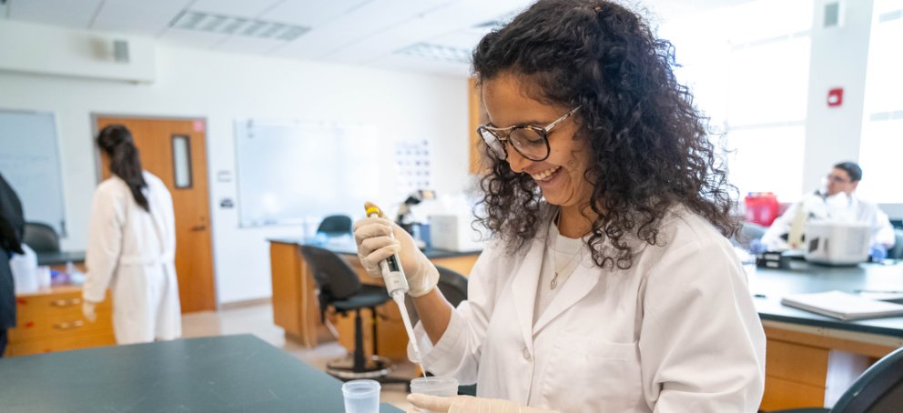 Student pippeting liquid into a container while smiling