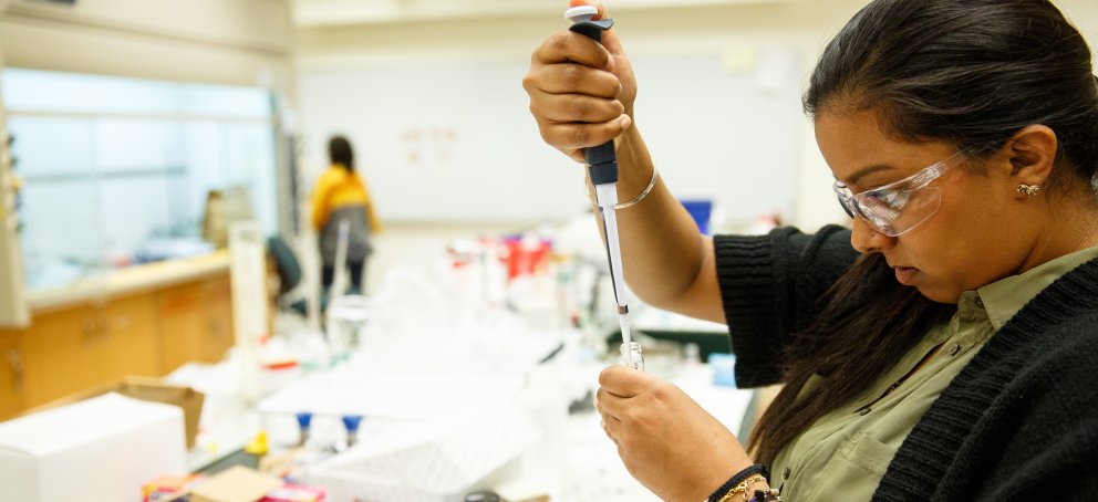 Student dropping chemicals into a beaker in a laboratory