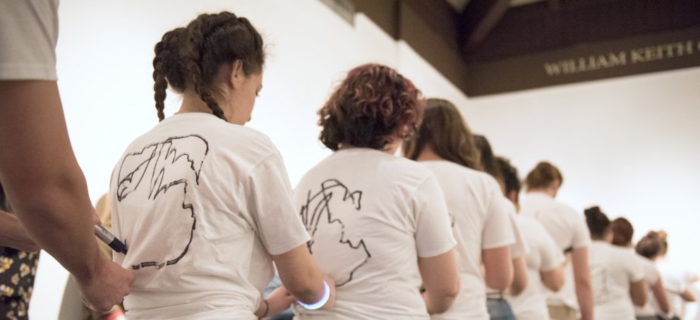 Students drawing on the backs of other student's shirts as part of performing art piece. 