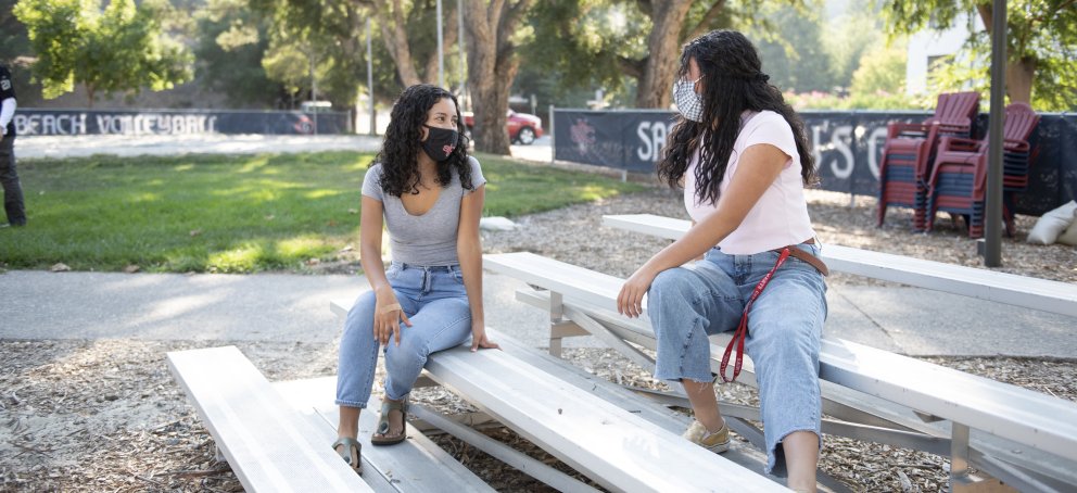 Two students sitting and talking on benches with masks on