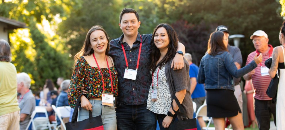 Three people smile in front of trees at twilight