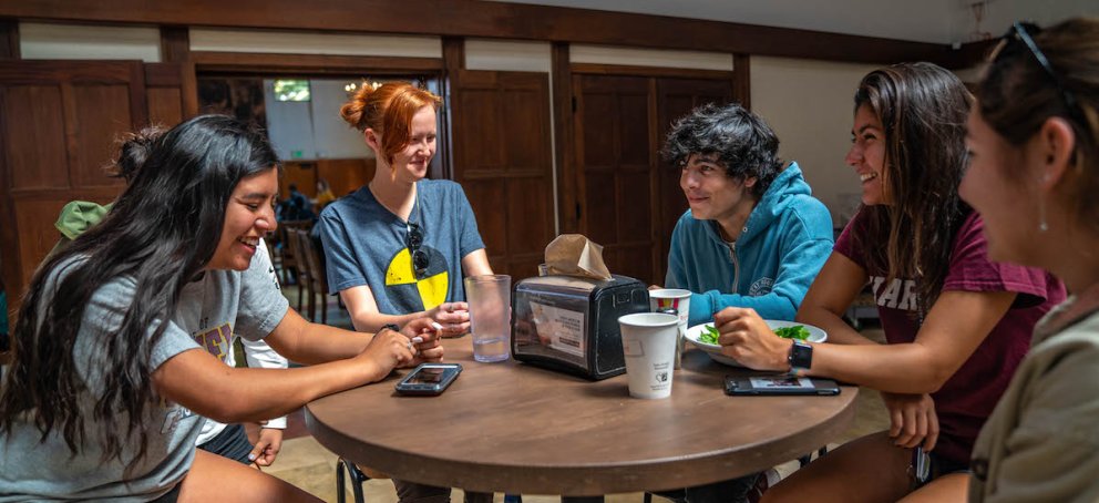 Five students in the dining hall, around a cafe table