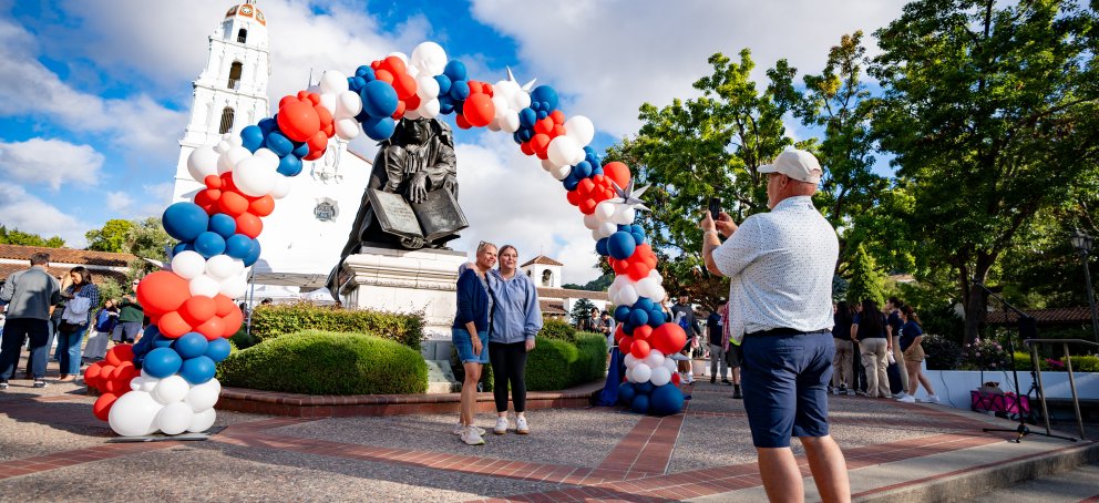 Dad taking picture of daughter under balloon arch during weekend of welcome