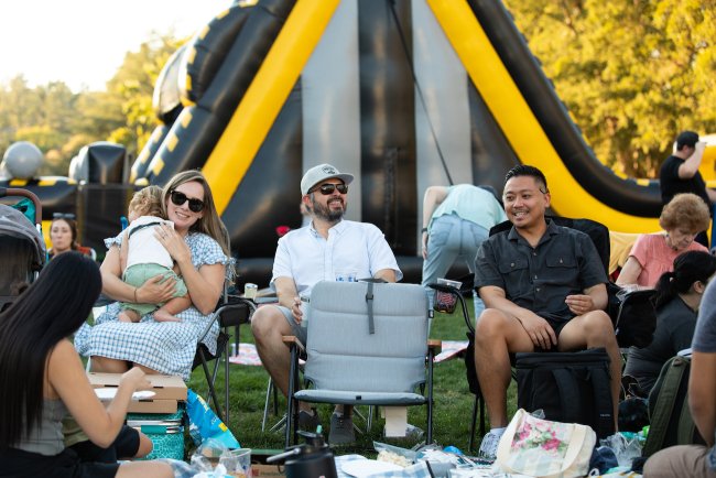 Three adults, one holding a baby, sit in picnic chairs