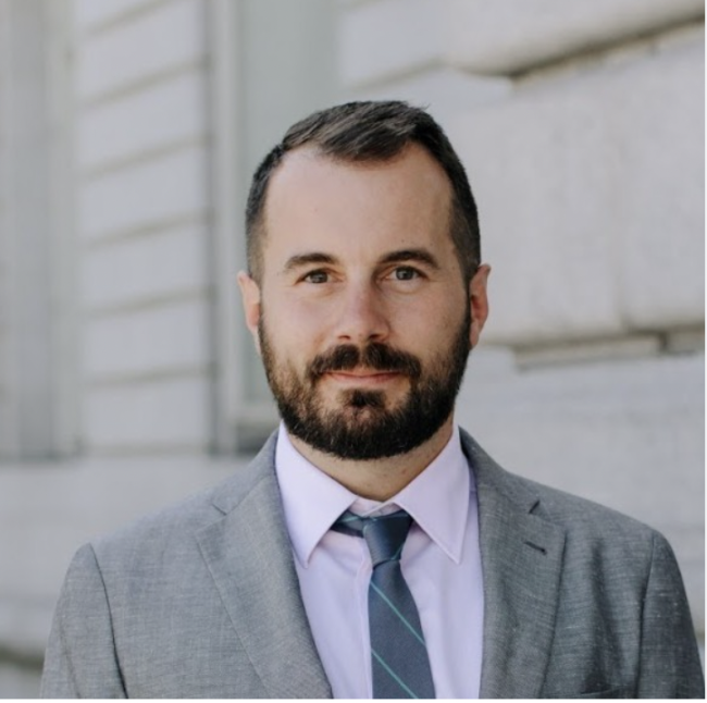 Beckett Finn dressed in a grey suit in front of a white building