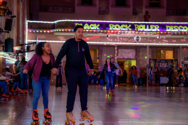 Amira Jones ‘25 holds on tightly to David Laines '25 while rolling around the rink during the SMC Roller Skating Night at the Church of 8 Wheels in San Francisco. / Photo By Francis Tatem