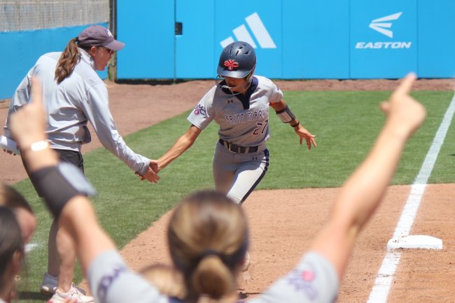 Softball payer Mia Zabat rounds third and coach Sonja Garrett congratulates her in May 2025