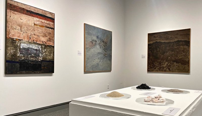Installation image of From the Ground Up showing paintings and earth materials of asphalt, gypsum and sand.
