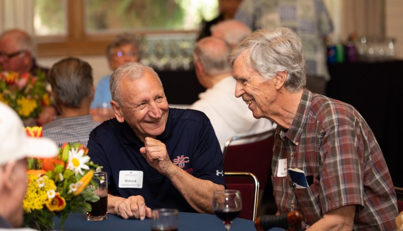 Two alumni share a laugh sitting around a table