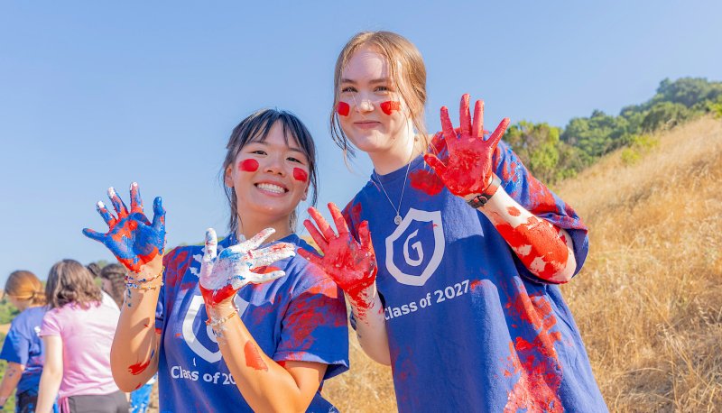 Two female students paint the SMC and smile at camera