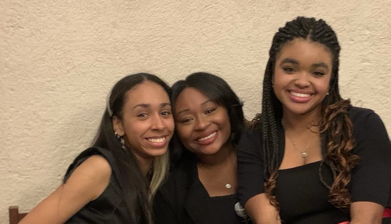 Three SMC females dressed in black dressy clothes smile at the camera.