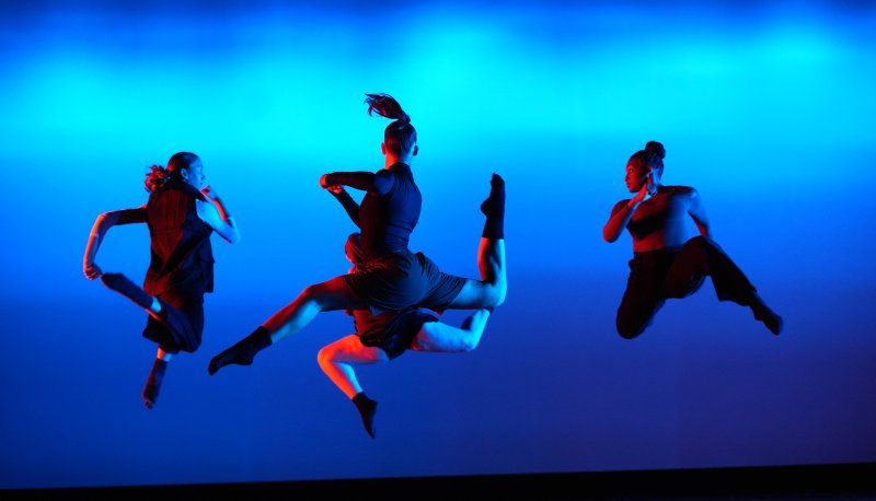 Shadowed dancers leaping in a circle with a bright blue background.