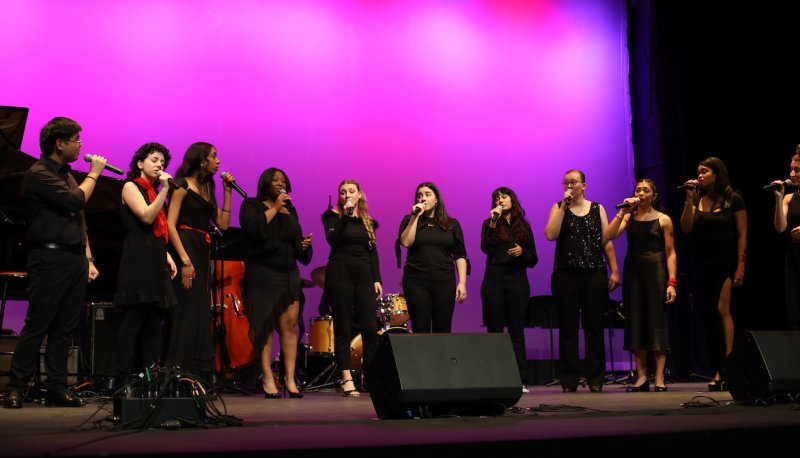 Jazz singers dressed in black with red accessories sing on LeFevre Stage with a purple hue on the cyc behind them.