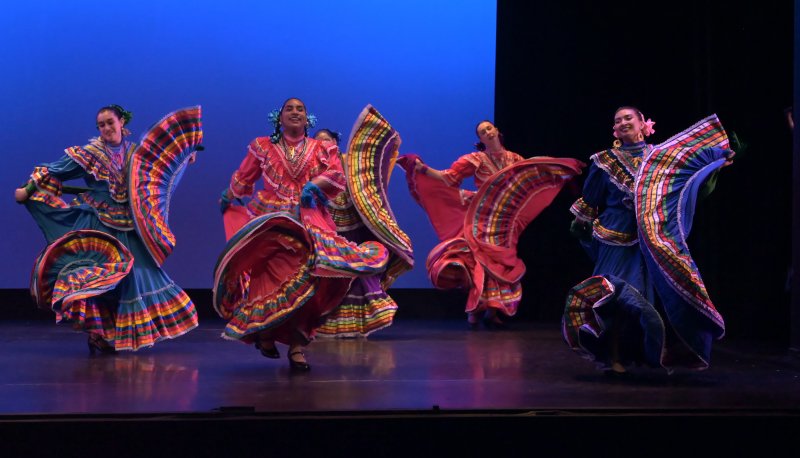 baile folklorico students dance on a stage with colorful skirts swirling around