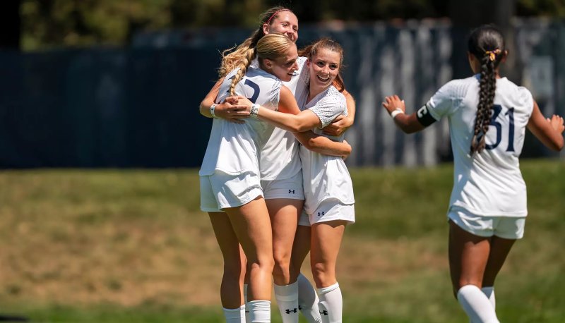 Four women's soccer players celebrate a victory in fall 2025