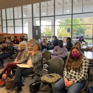 A group of students, faculty, and staff gathered on the second floor of the library listening to a poetry reading.