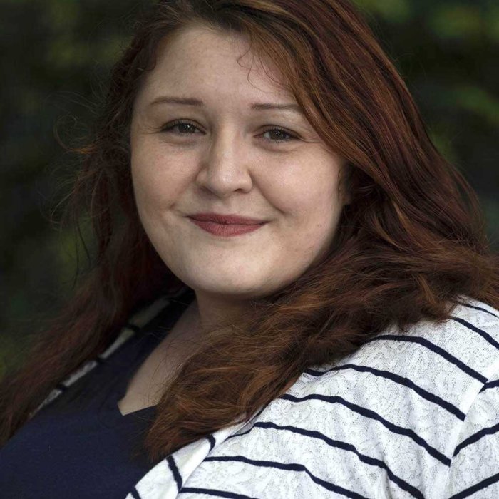 A red-headed woman with a striped black-and-white shirt against faded shrubbery