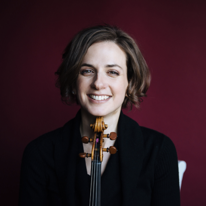 Liana Bérubé against a red background, smiling, and resting her chin on a violin