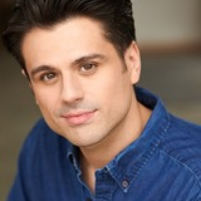 A headshot of Alexander McDaniel, wearing a blue collared shirt