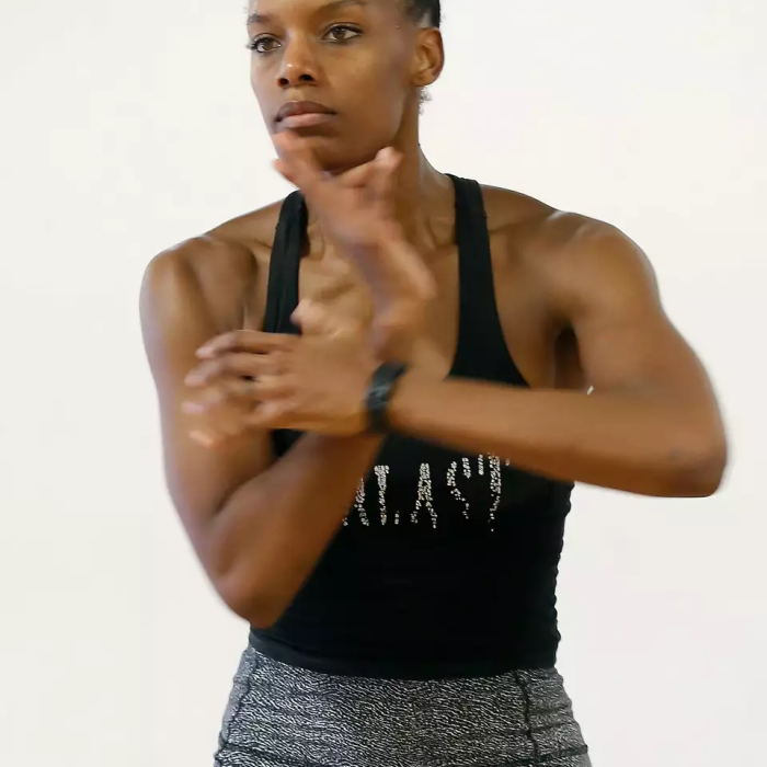 Crystaldawn Bell, a dancer in the midst of a move with blurred arms. Behind her, a white wall