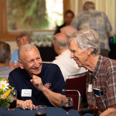 Two alumni share a laugh sitting around a table