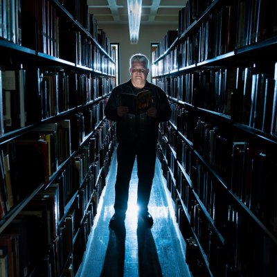 Norm Partidge in library stacks with dramatic lighting, October 2023