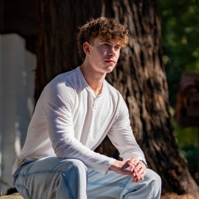 Saint Mary's student Kian Tanner '27 seated on a bench by a redwood