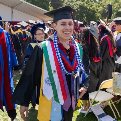 Isaac, in graduation cap and gown, smiles at the camera amongs dozens of his classmates