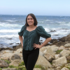 A woman is posing in front of a rocky beach