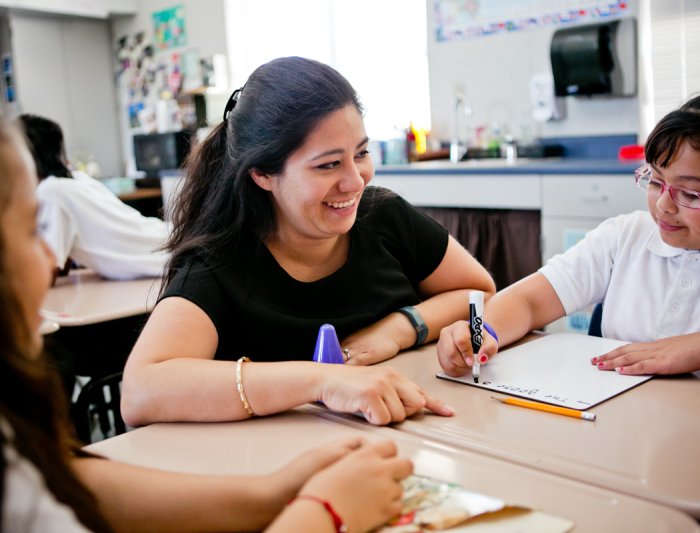 A teaching smiling at a student writing on a white board at a desk