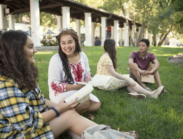 Two women in class sitting on the grass discussing a book