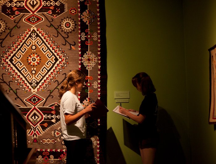 photo of two students taking notes in front of a piece of textile art in the museum