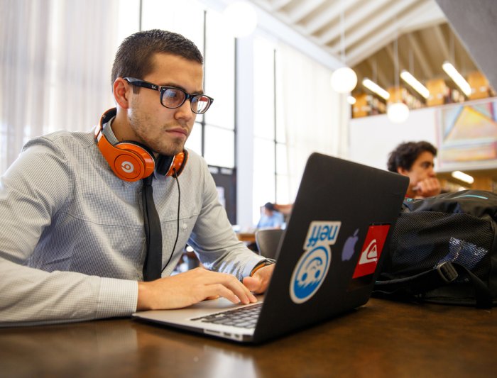 A student with headphones on working at a laptop in the library