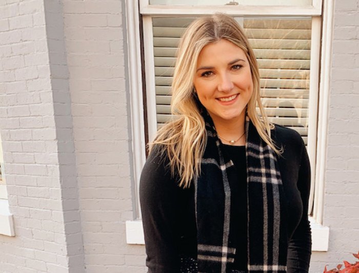 Alumna in black suit portrait photo standing before an office window