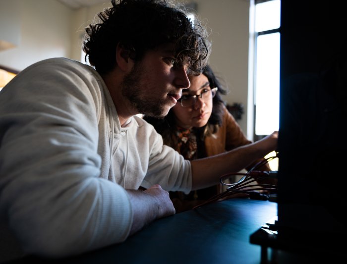 A man and woman look at a computer screen in low lighting