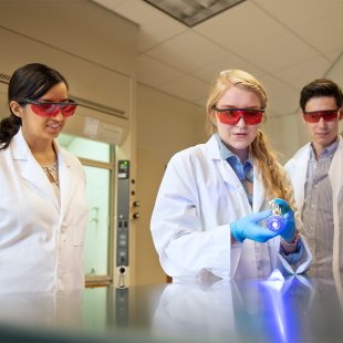 students in lab coats and protective glasses work on an experiment